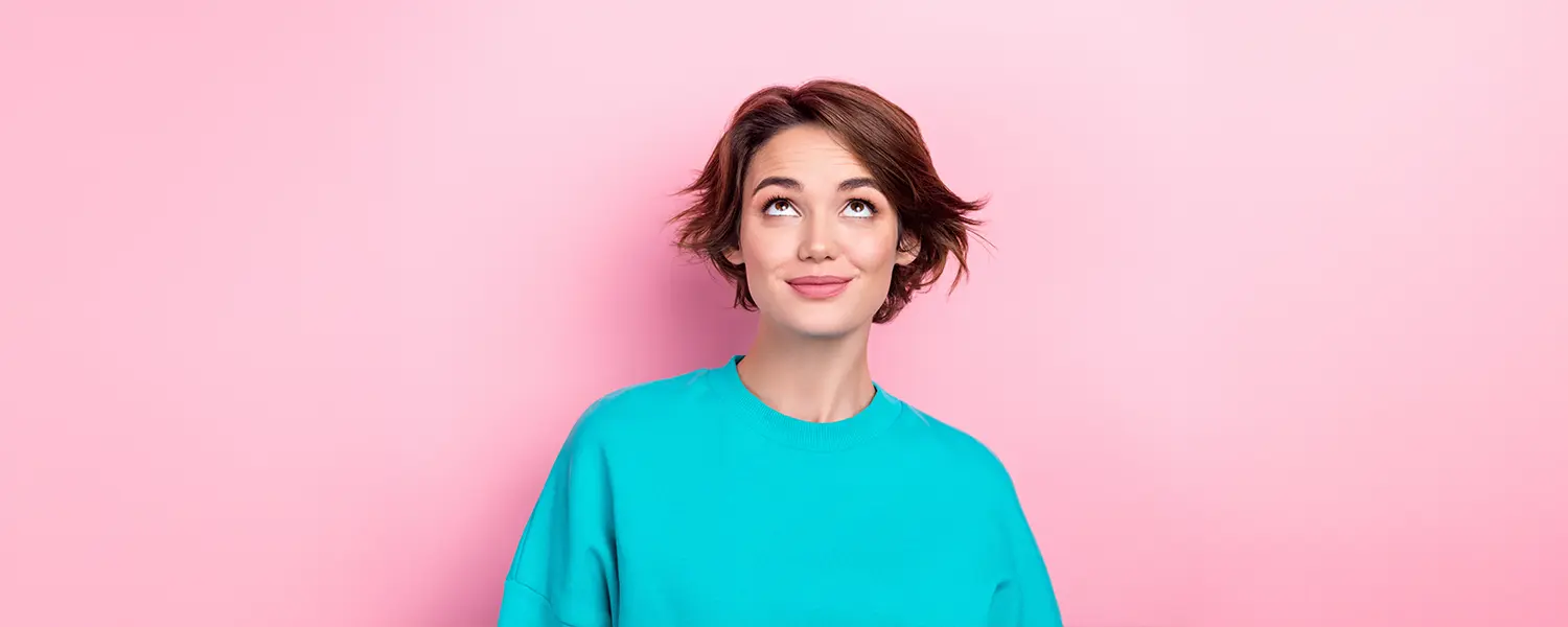 A person with short brown hair in a turquoise shirt looks thoughtfully upward against a pink background.