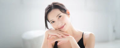 Dark-haired person in black top rests chin on hands; serene