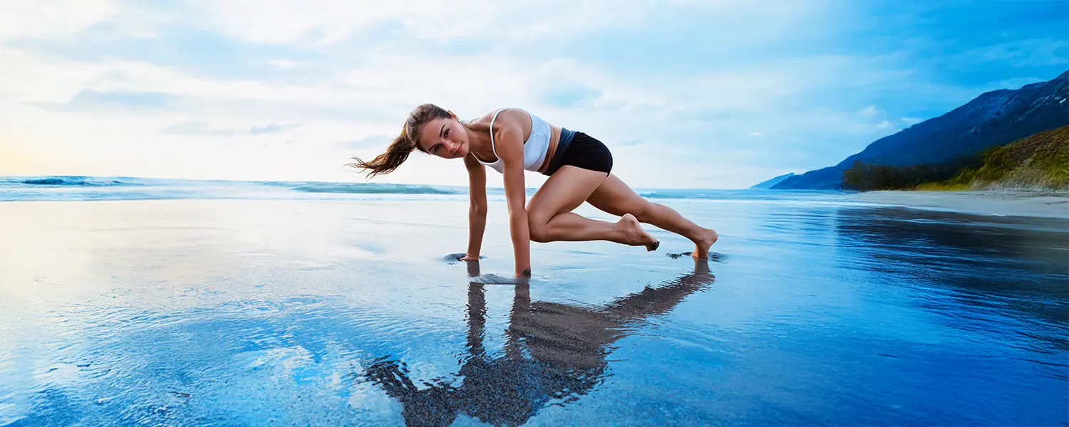 plastic-surgery-hawaii-hero-1 A woman exercises on a beach in a mountain climber pose