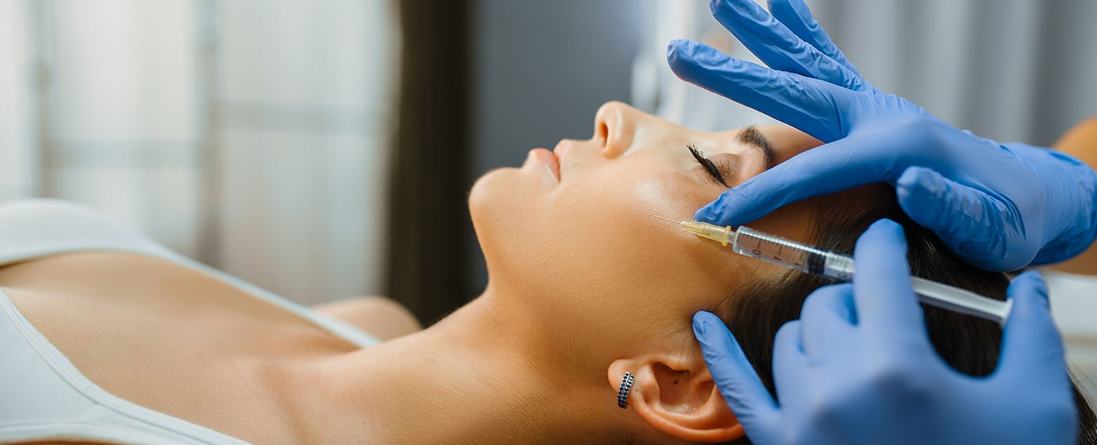A professional injects a substance into a person's cheek in a clinical setting.