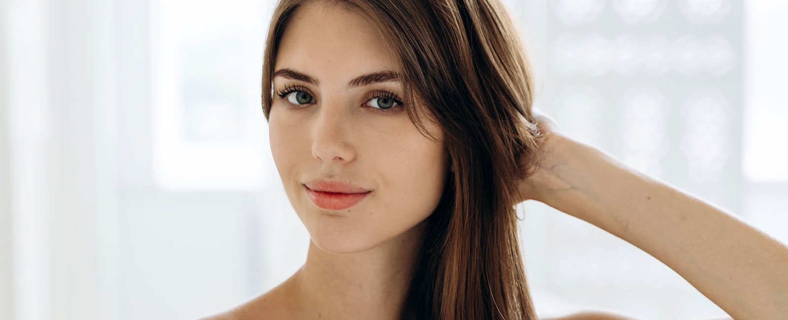 plastic-surgery-hawaii-hero-1 A person with long brown hair and blue eyes touches their hair