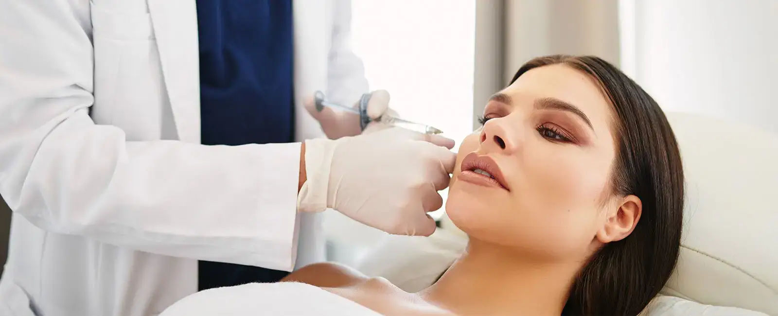 plastic-surgery-hawaii-hero-1 A professional gives a facial injection to a relaxed woman in a treatment room.