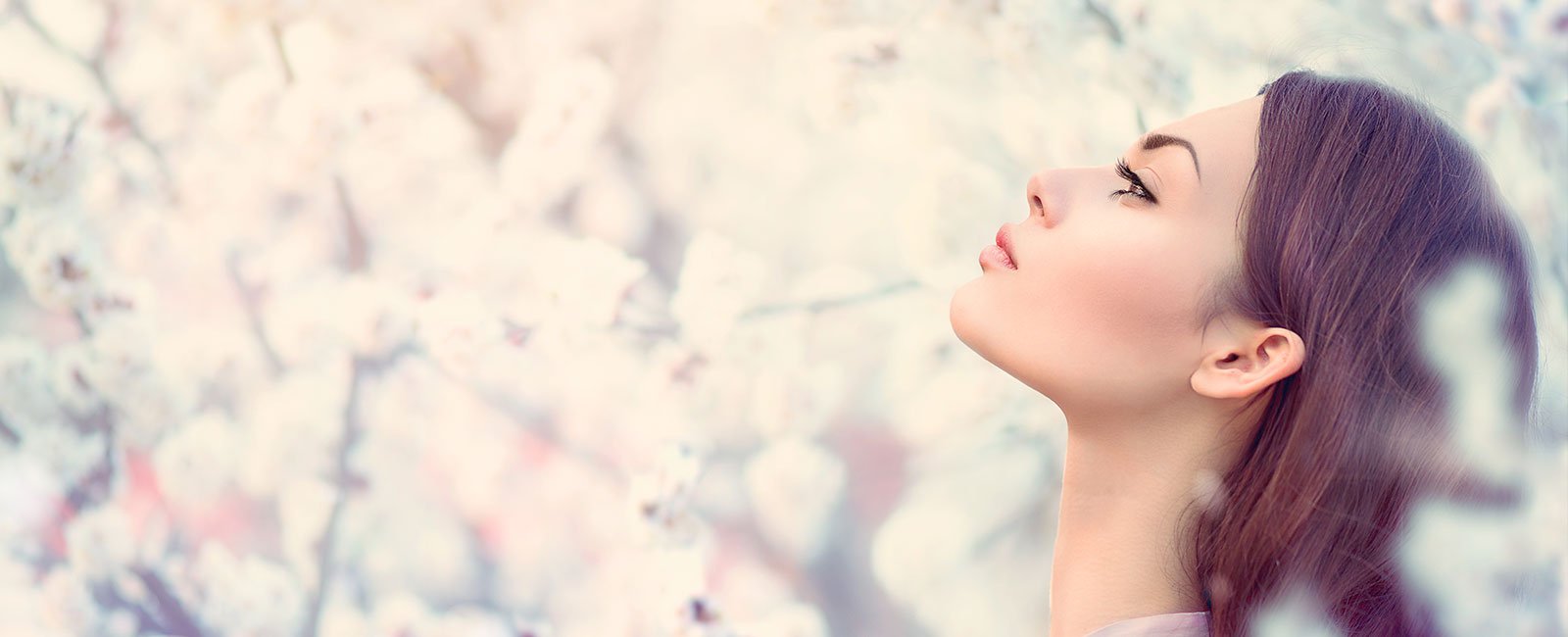 A serene woman with long brown hair is shown in profile against a blurred background of white flowers.